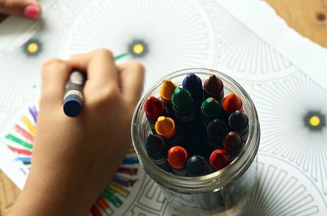child's hand holding a crayon with jar of crayons next to it