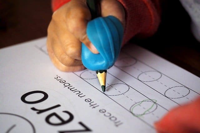child's hand with a pencil and finger guide tracing letter