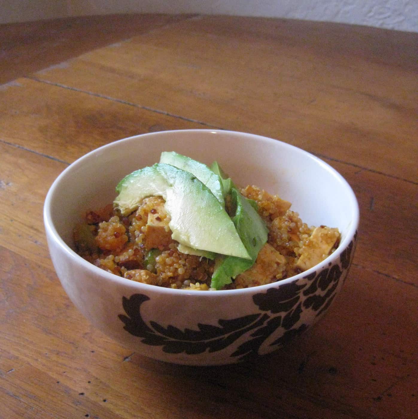 bowl with vegetarian tofu, quinoa, and avocado slices on table