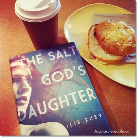 Ilie Ruby's novel The Salt God's Daughter on table, coffee cup, bagle on plate