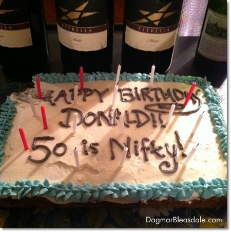 50th birthday party sheet cake on table, wine bottles in the back