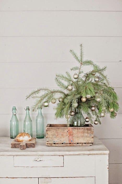 pine tree branches in bottle with simple ball ornaments, in crate on table