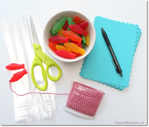 supplies for kids valentines, candy fish, note cards, cellophane bags, scissors, pen on table