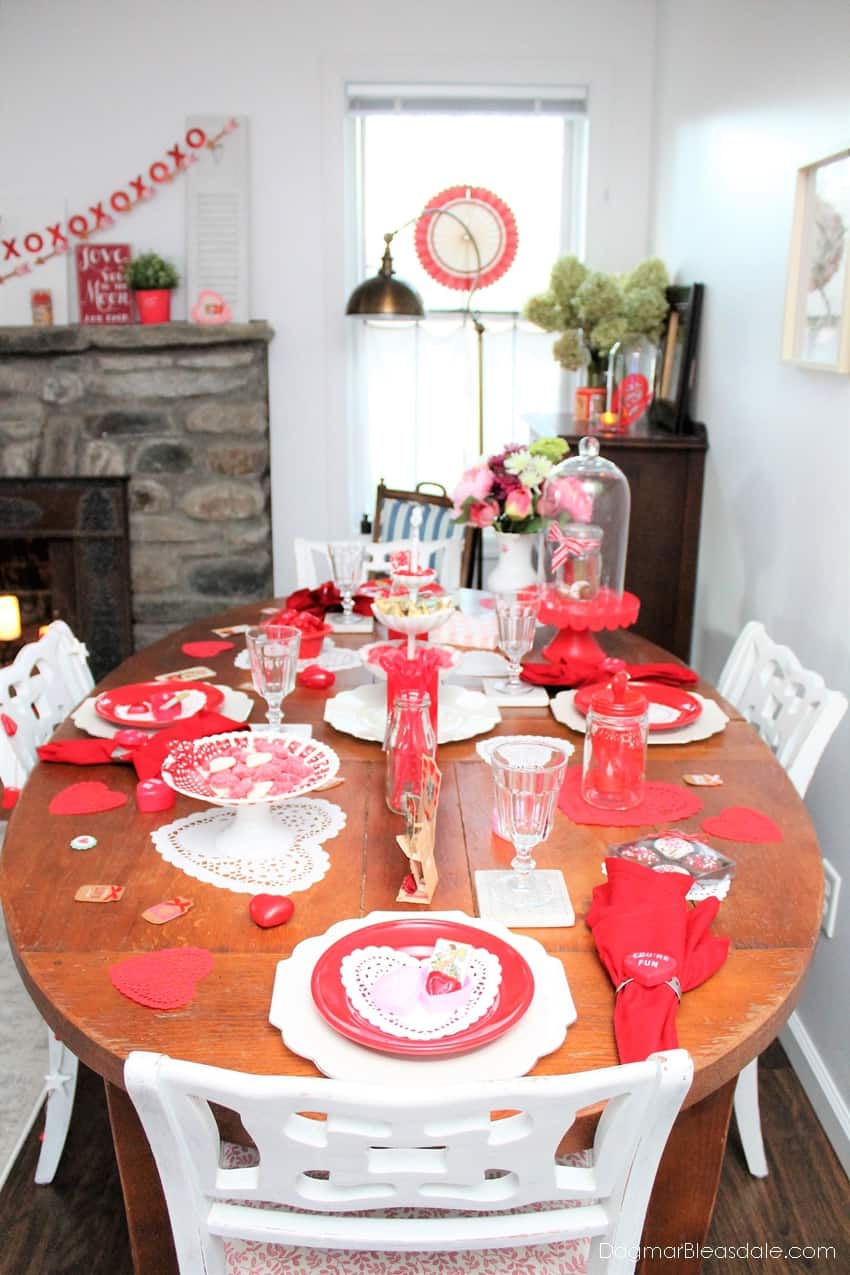 Valentine's Day decor of table with red plates and napkins, candy, banner over fireplace