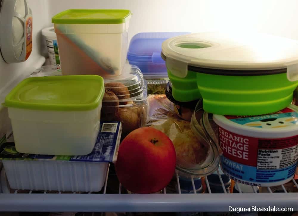 several plastic containers with food on refrigerator shelf