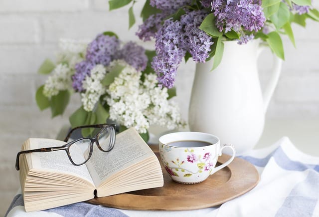 book with glasses, coffee cup with coffee, pitcher with flowers
