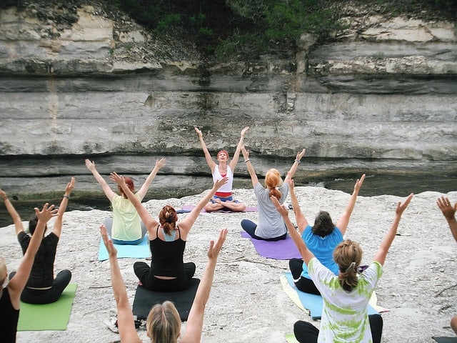 group of women doing yoga sitting on large rock in front of rock wall