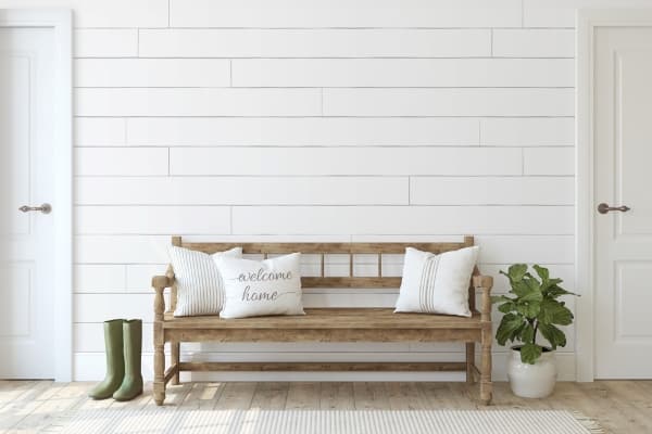 brown bench in front of shiplap wall, plant and rainboots
